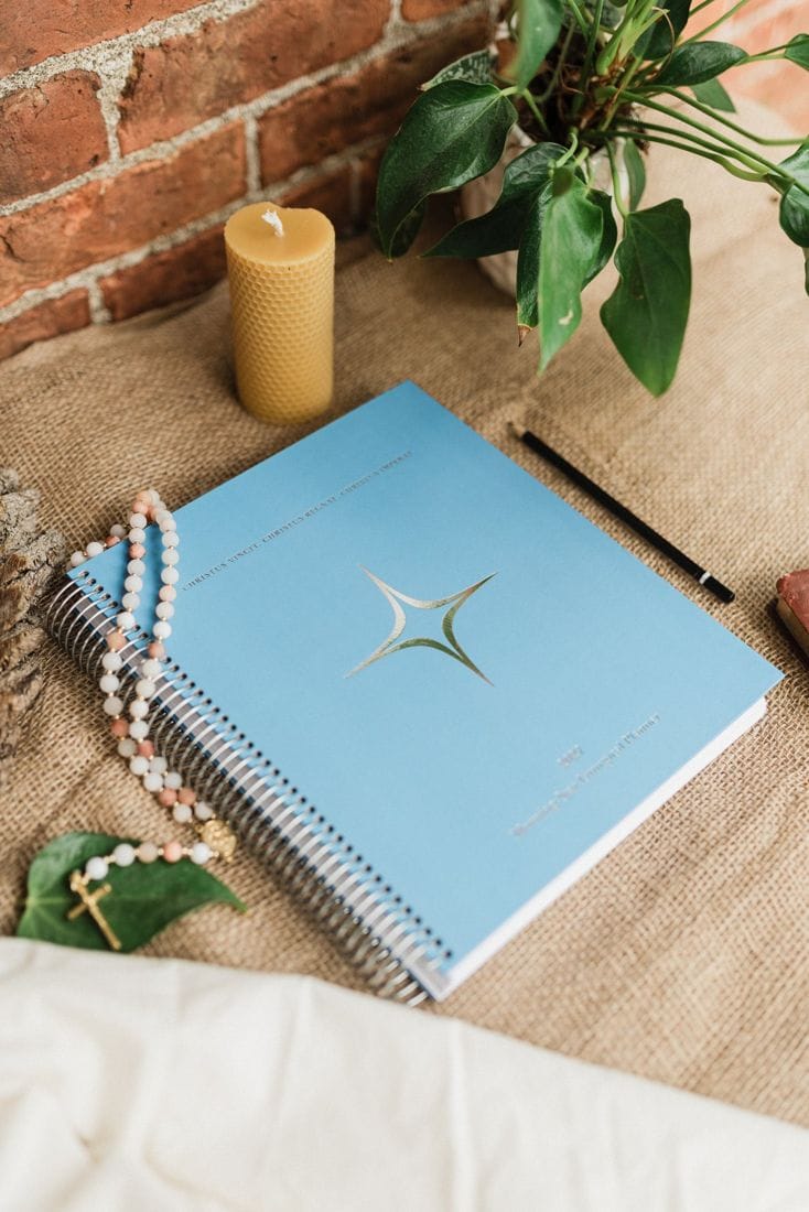 The planner's blue cover with its Morning Star, beside a beeswax candle and a rosary