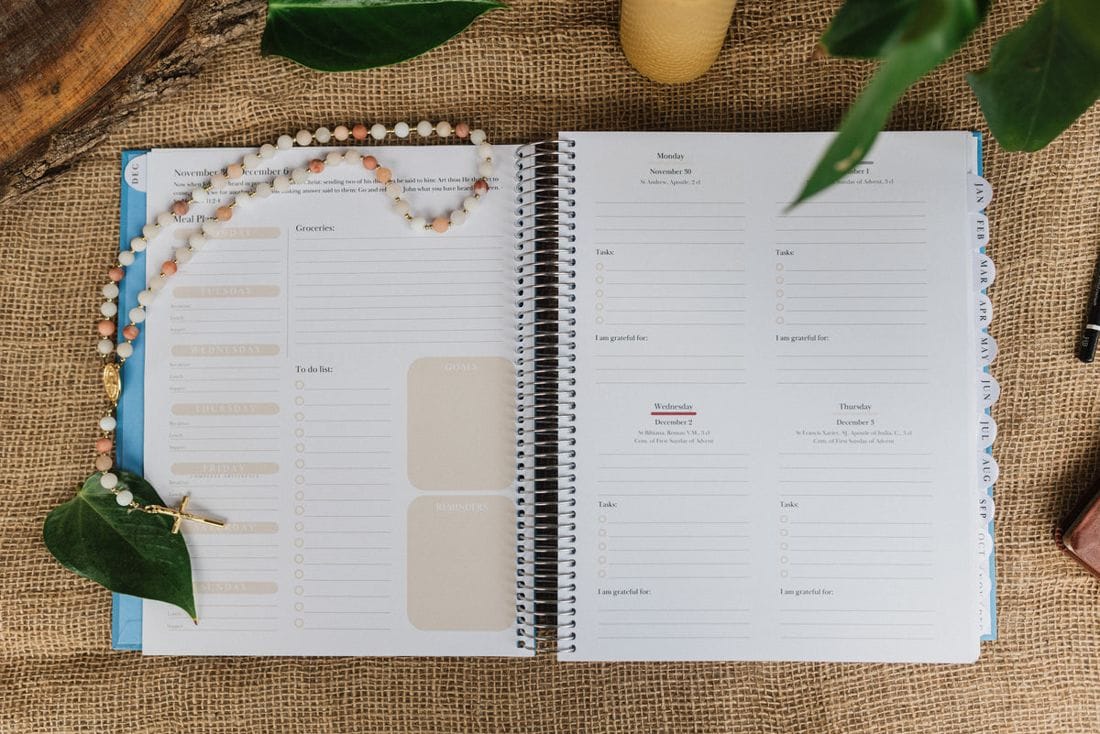 The planner open to a weekly spread, with a rosary and a beeswax candle beside it